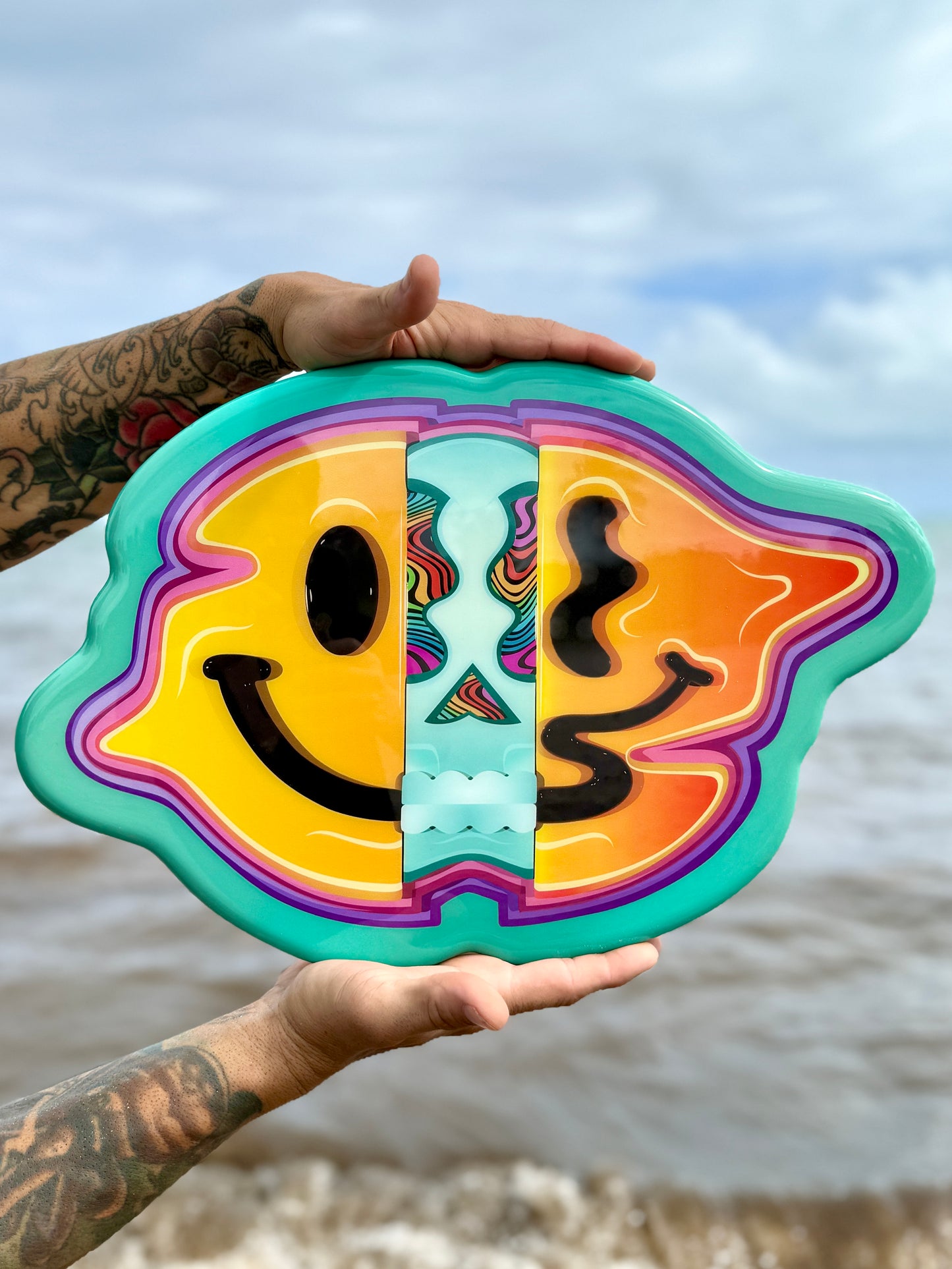 Colorful object with smiley face design held by a person against a beach background