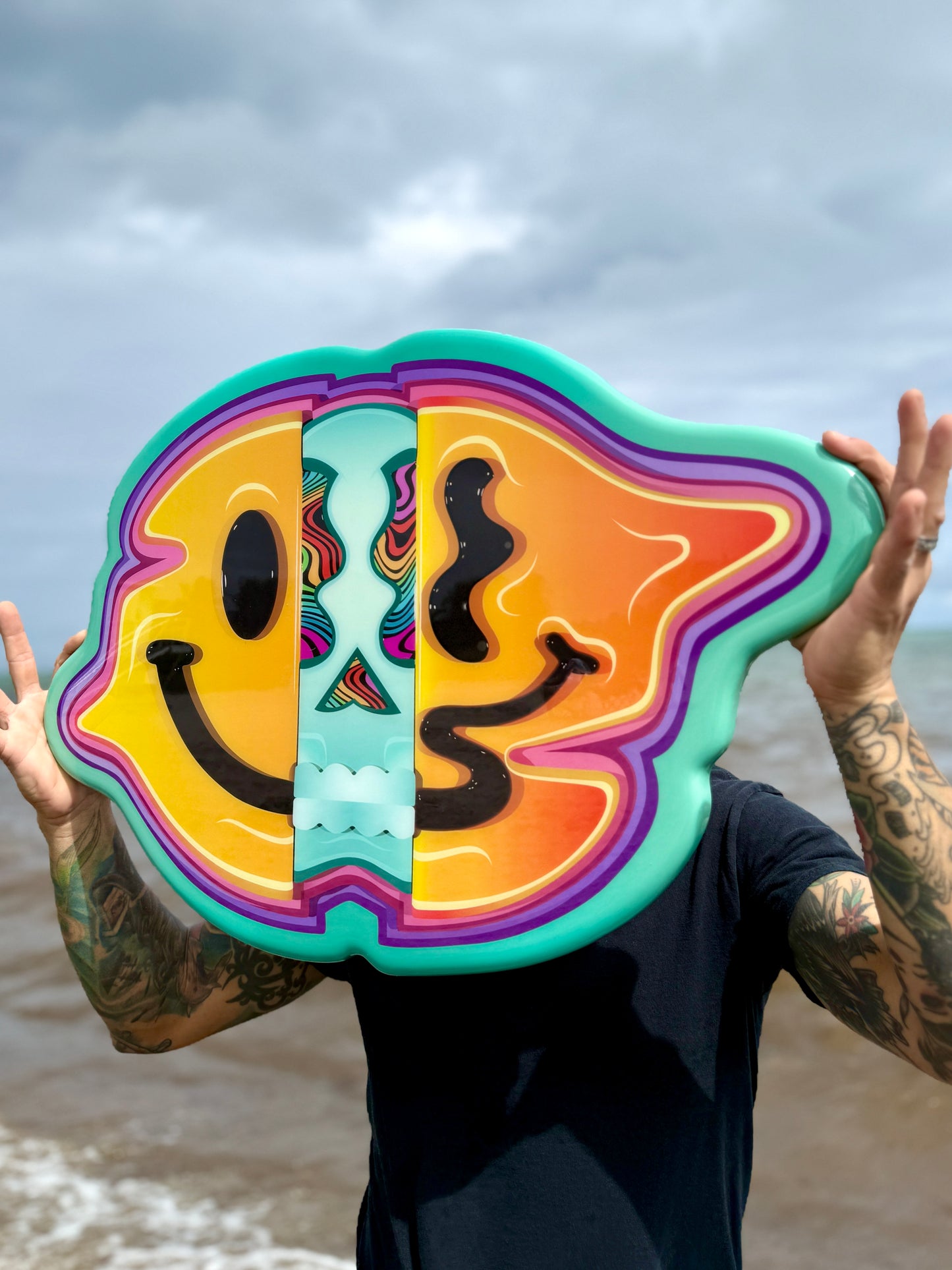 Person holding a colorful smiley face object with a beach background