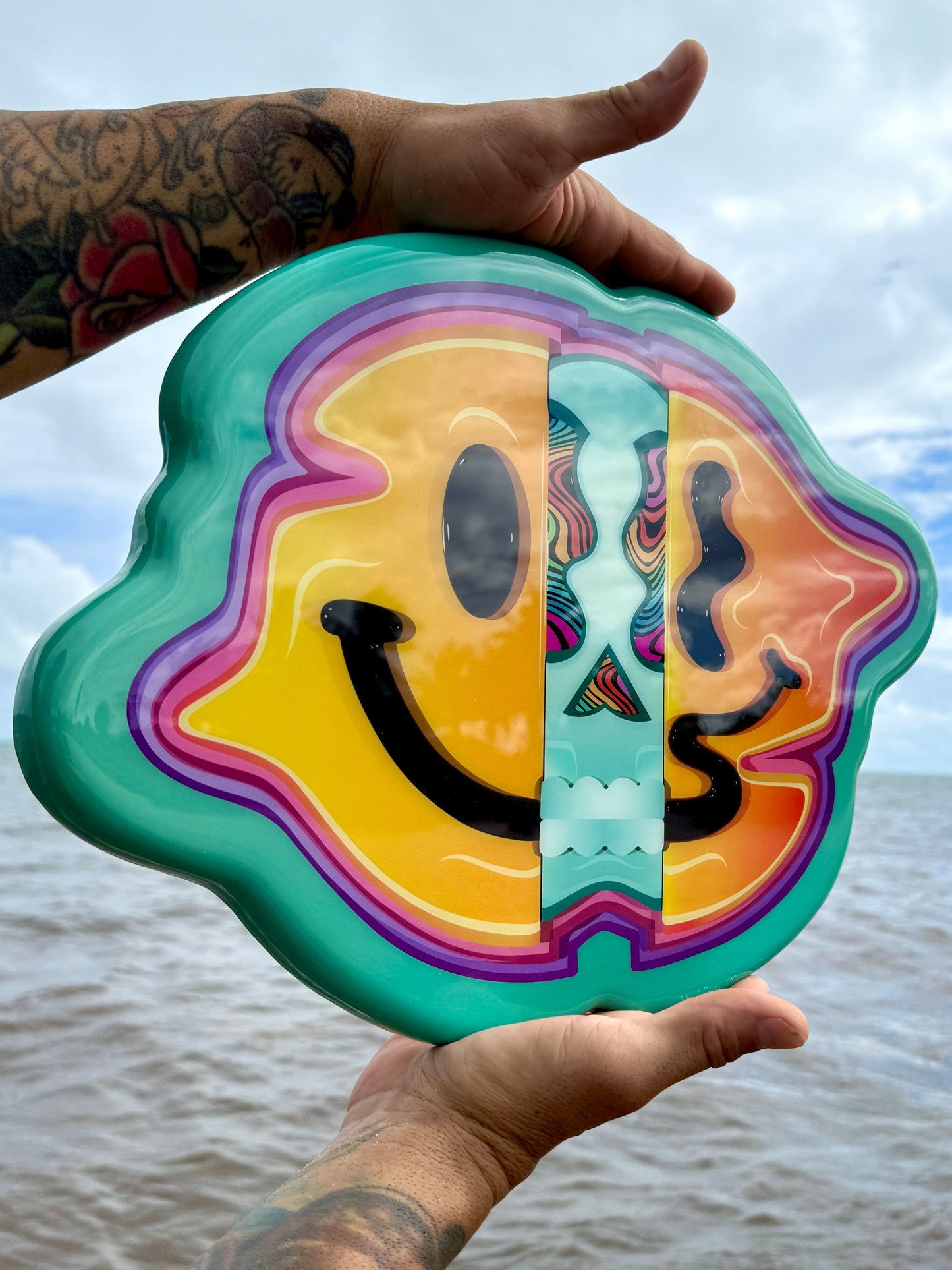 Colorful smiley face design held by a person with a beach background